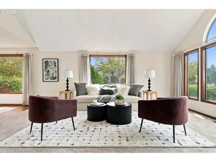 Staged living room with a cream sofa, two plum velvet chairs and black side tables beneath an arched window