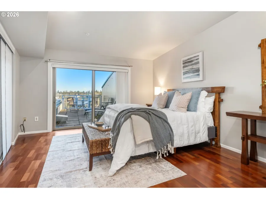 Penthouse condo bedroom staged with layered white bedding and a throw, with balcony doors and city views
