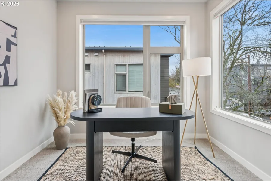 New-construction townhome room staged as a bright home office with a dark desk, white chair and floor lamp